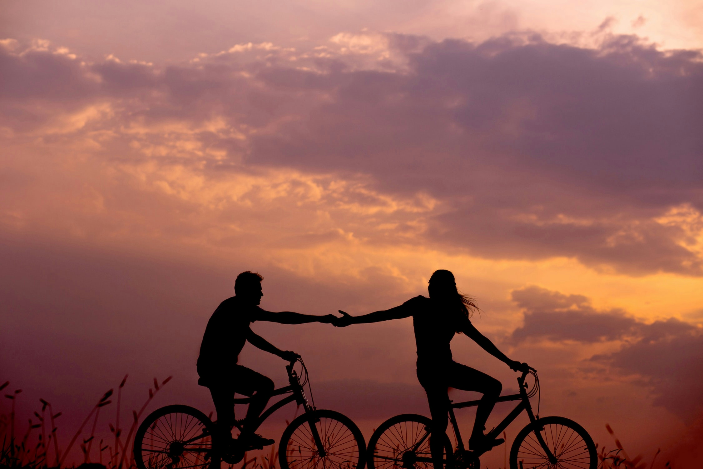 A couple riding bikes and reaching for each other